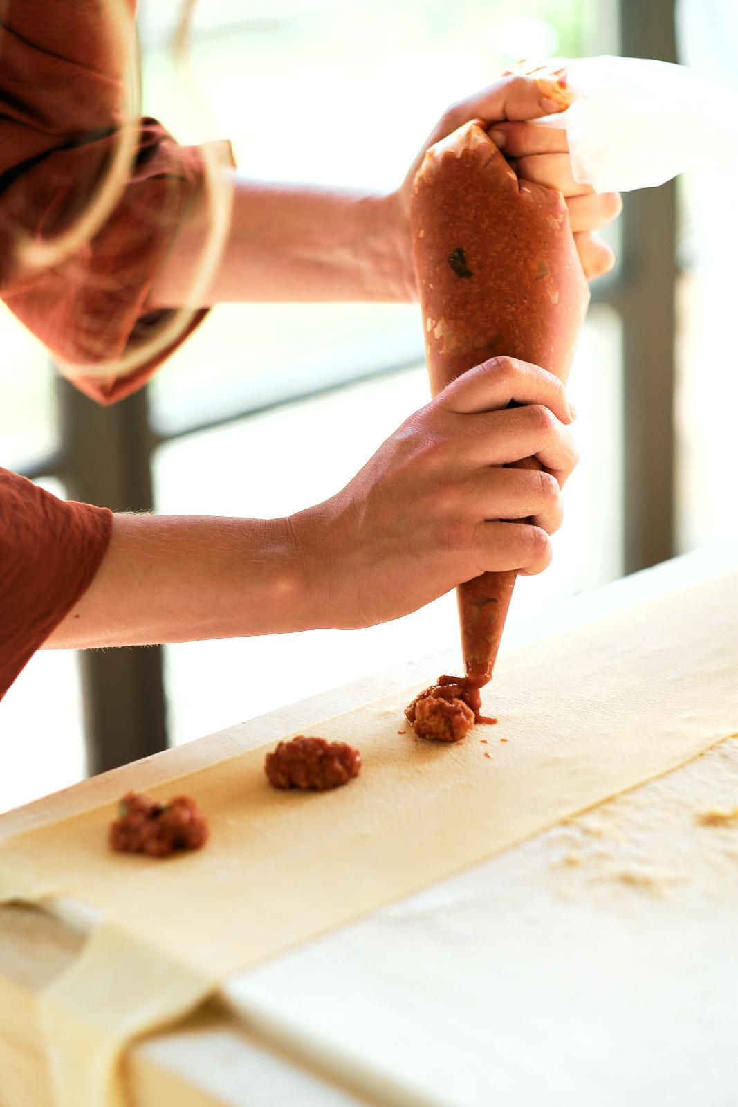 Close-up of hands piping filling onto fresh pasta dough