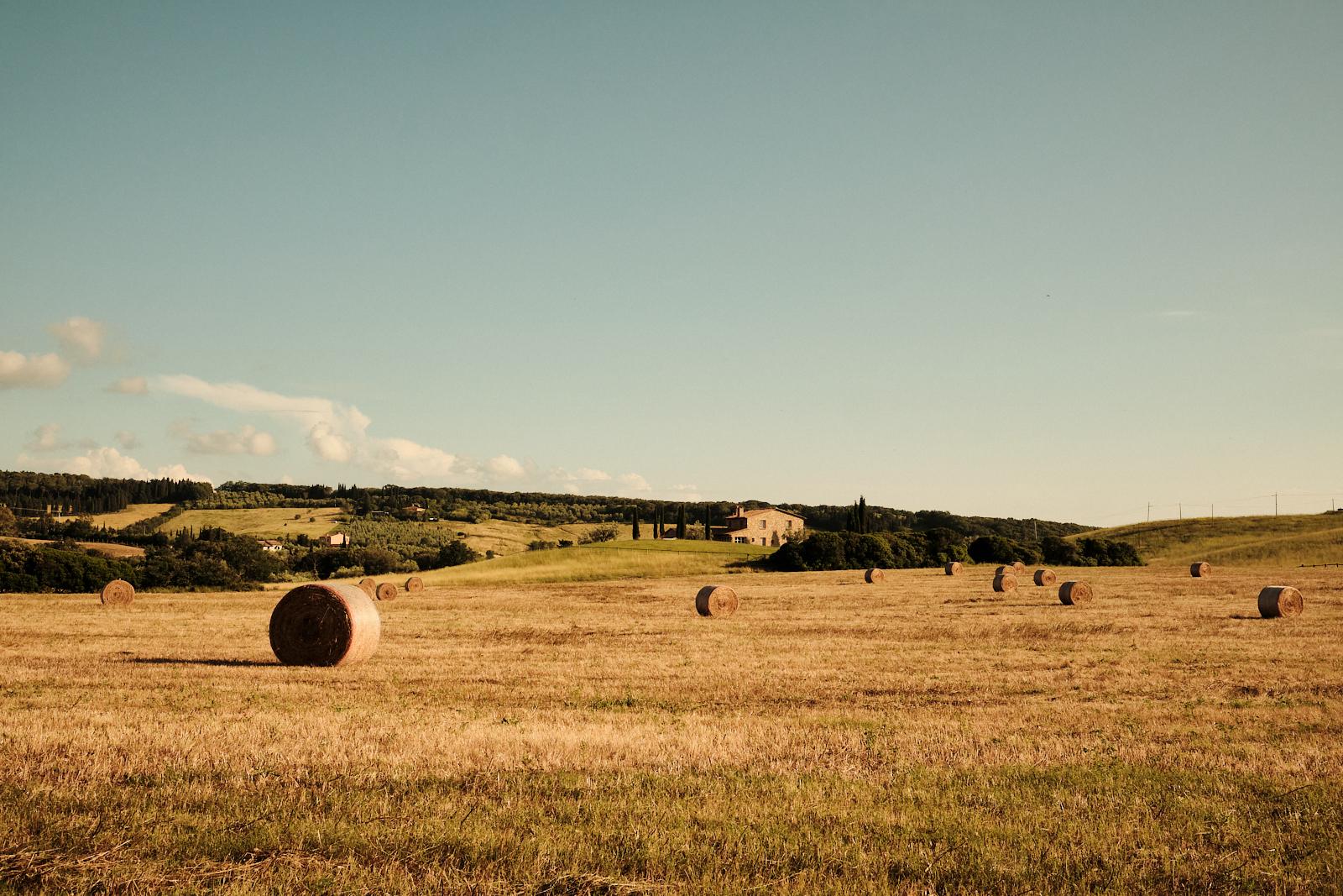 Hay bales in a Tuscan field with the estate visible on the hill behind