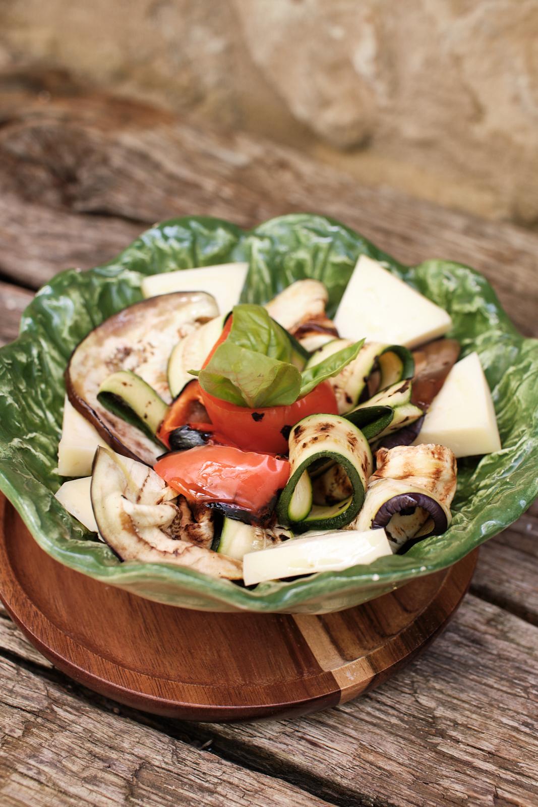A plate of grilled vegetables and cheese, served on a rustic table
