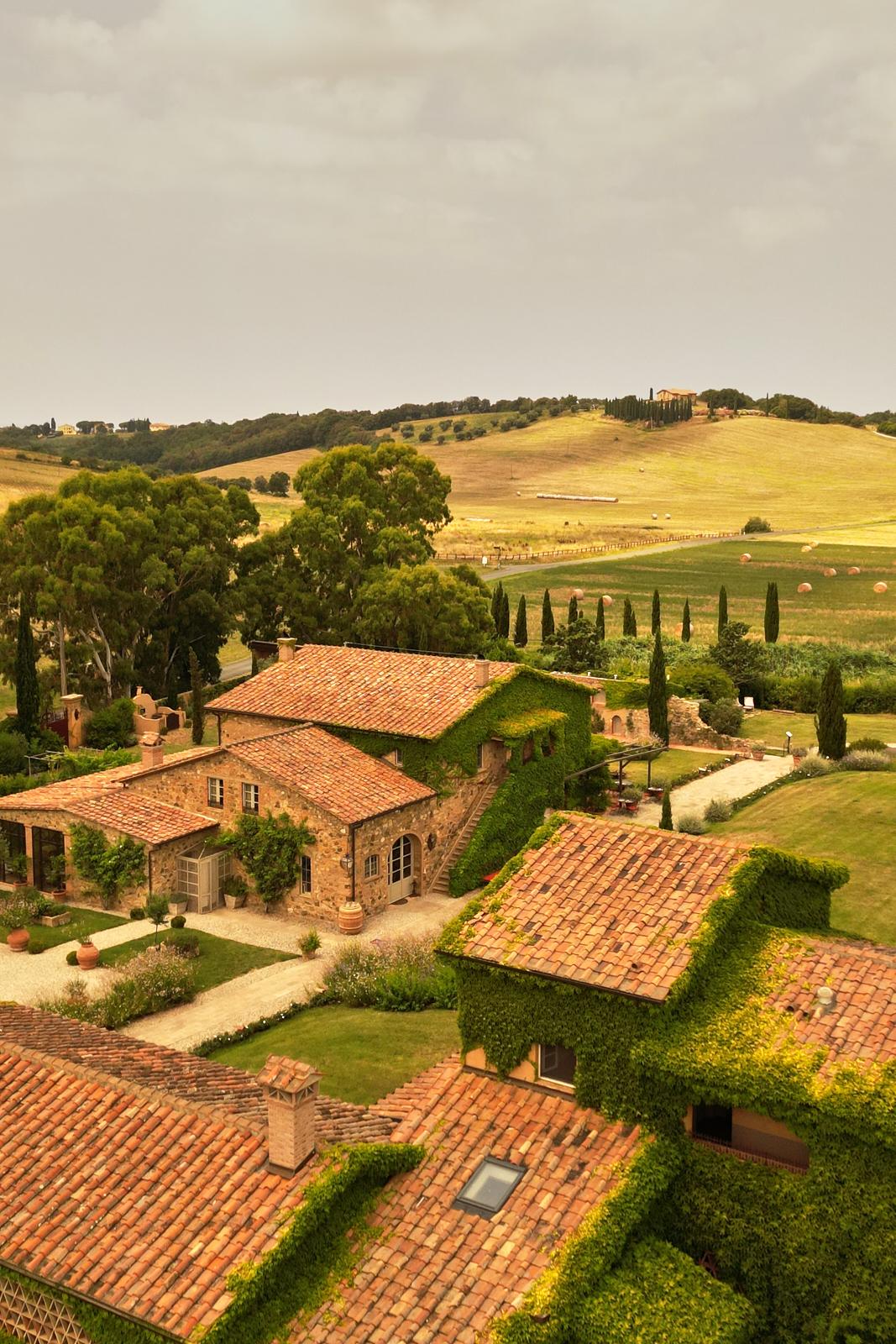 Aerial view of the ivy-covered stone villa and its grounds, Tuscan hills behind