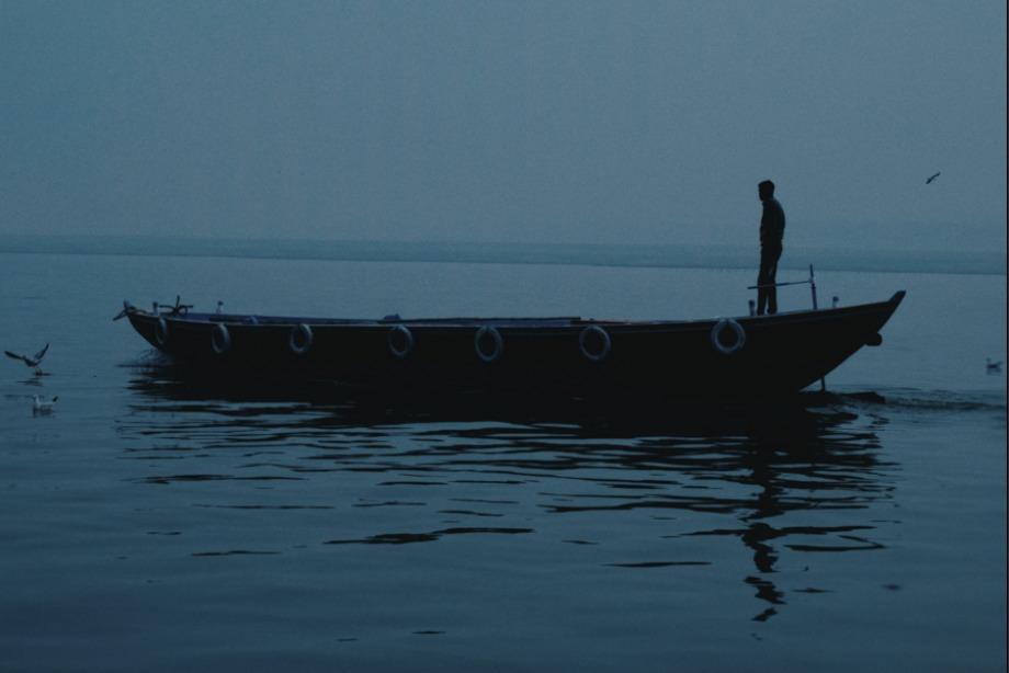 A boatman standing at dawn on the Ganges at Varanasi, silhouetted against still water