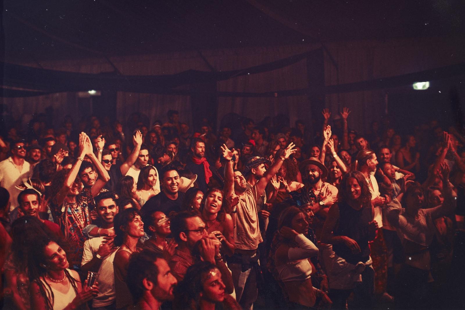 A red-lit crowd inside the marquee, hands raised