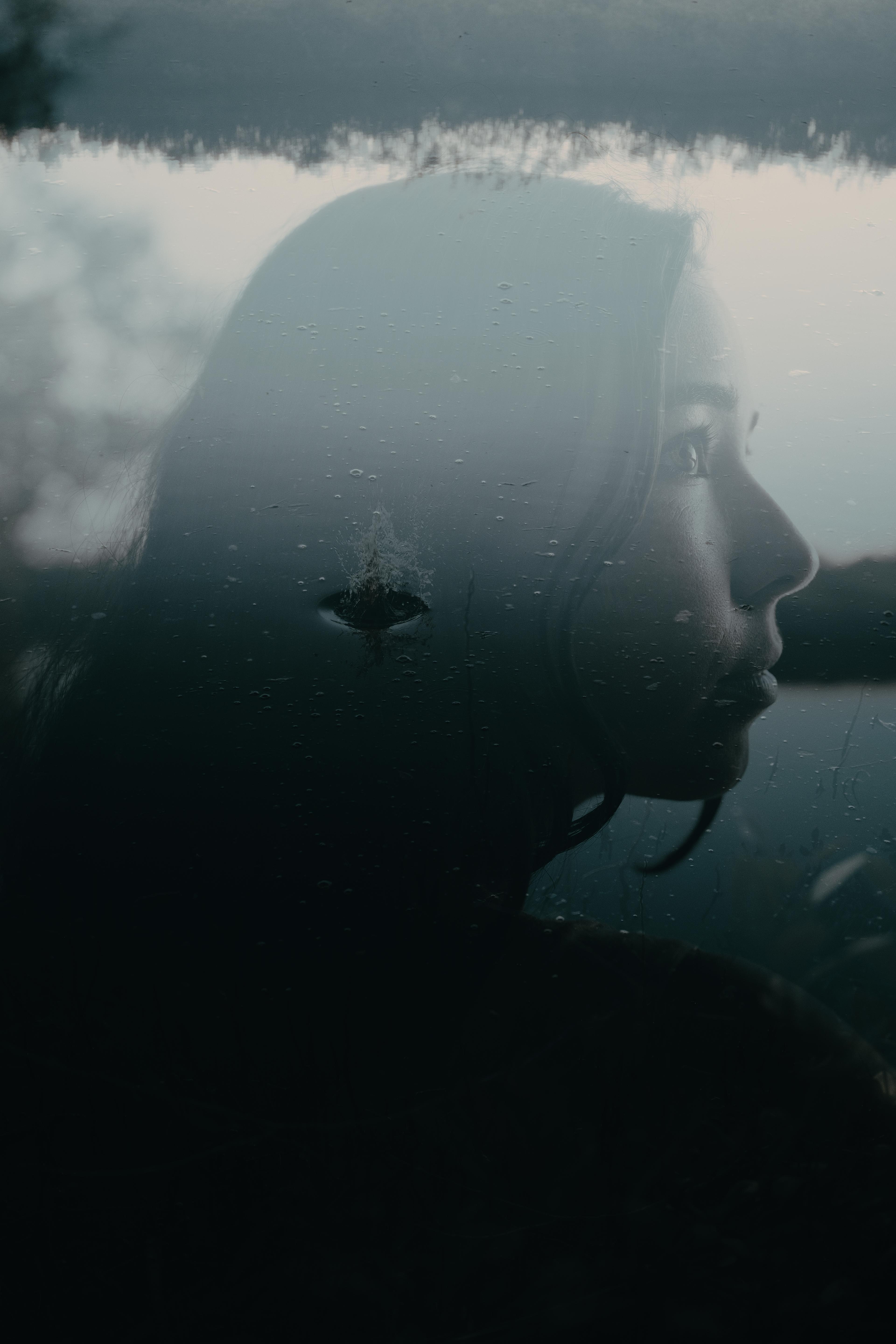 Double exposure of a woman's profile looking out over still water, overlaid with ripples and a raindrop's splash