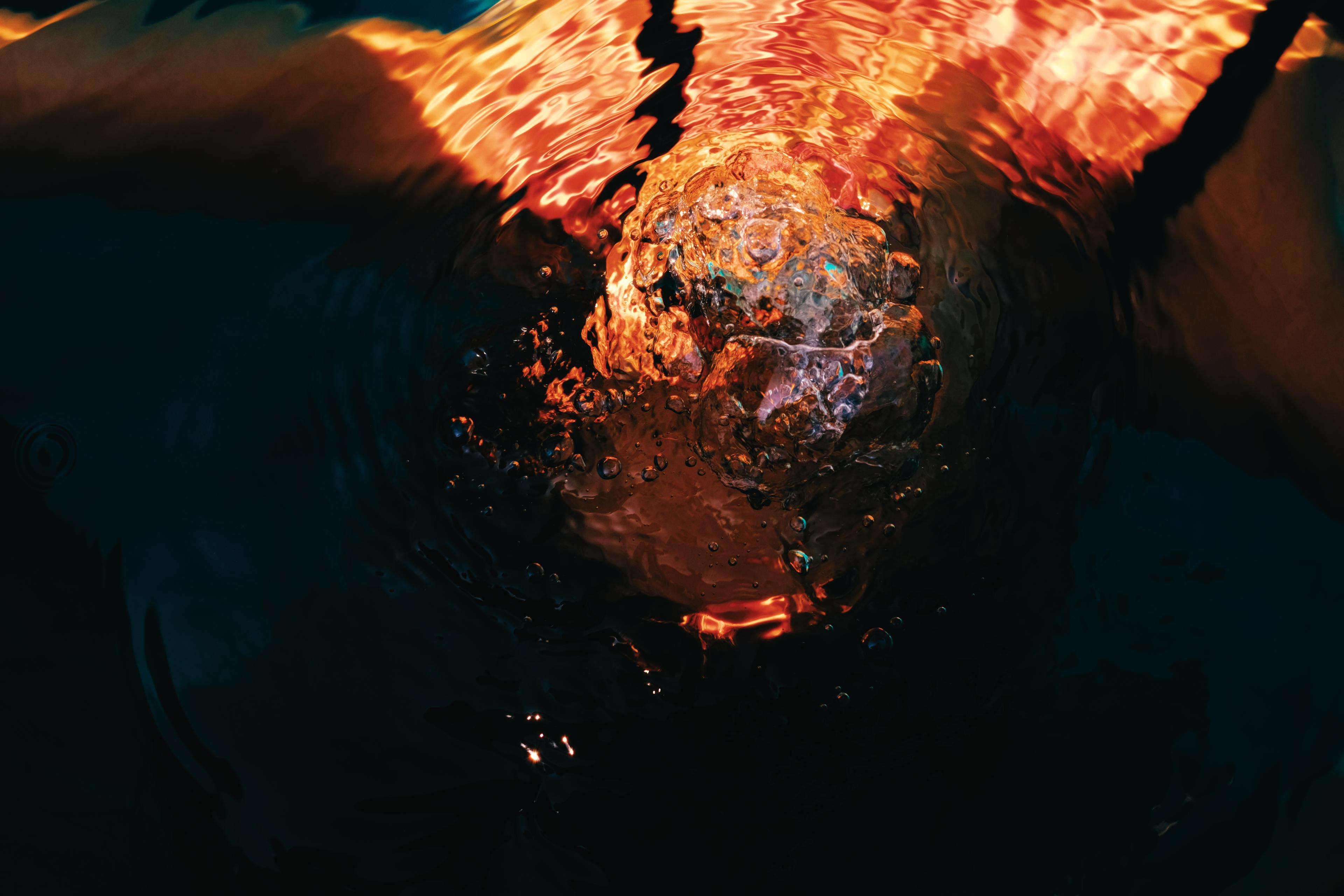 Close-up of dark water with a fiery orange reflection and rising bubbles at its centre