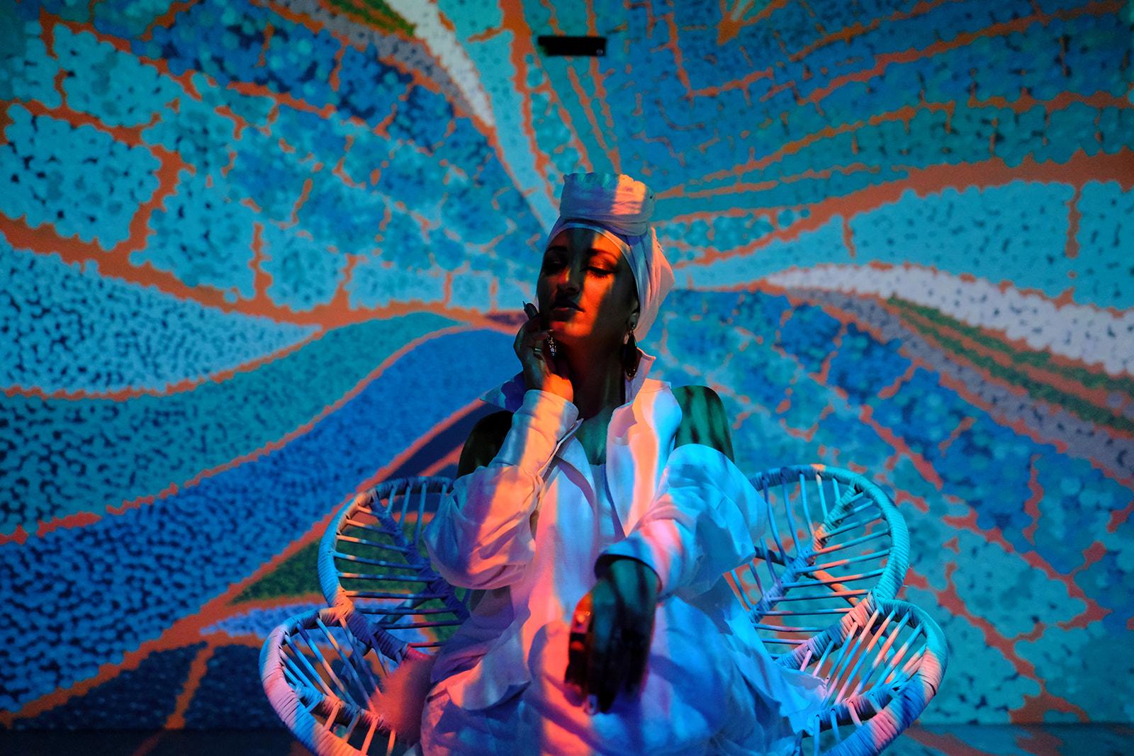Juman seated in a rattan chair against a wide projected blue and orange mural