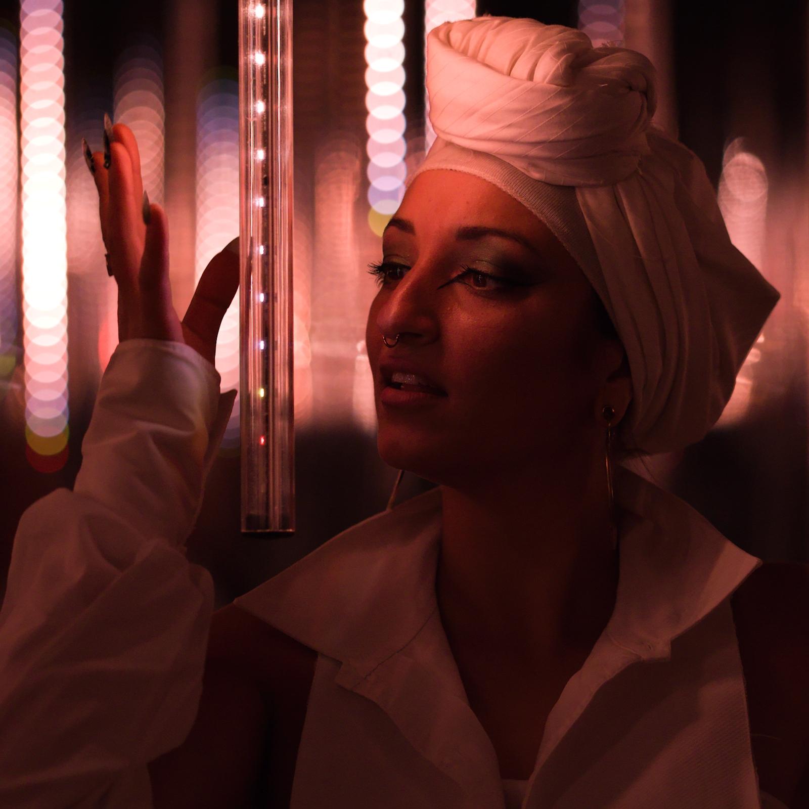 Juman in a white headwrap, lit by neon tube lights