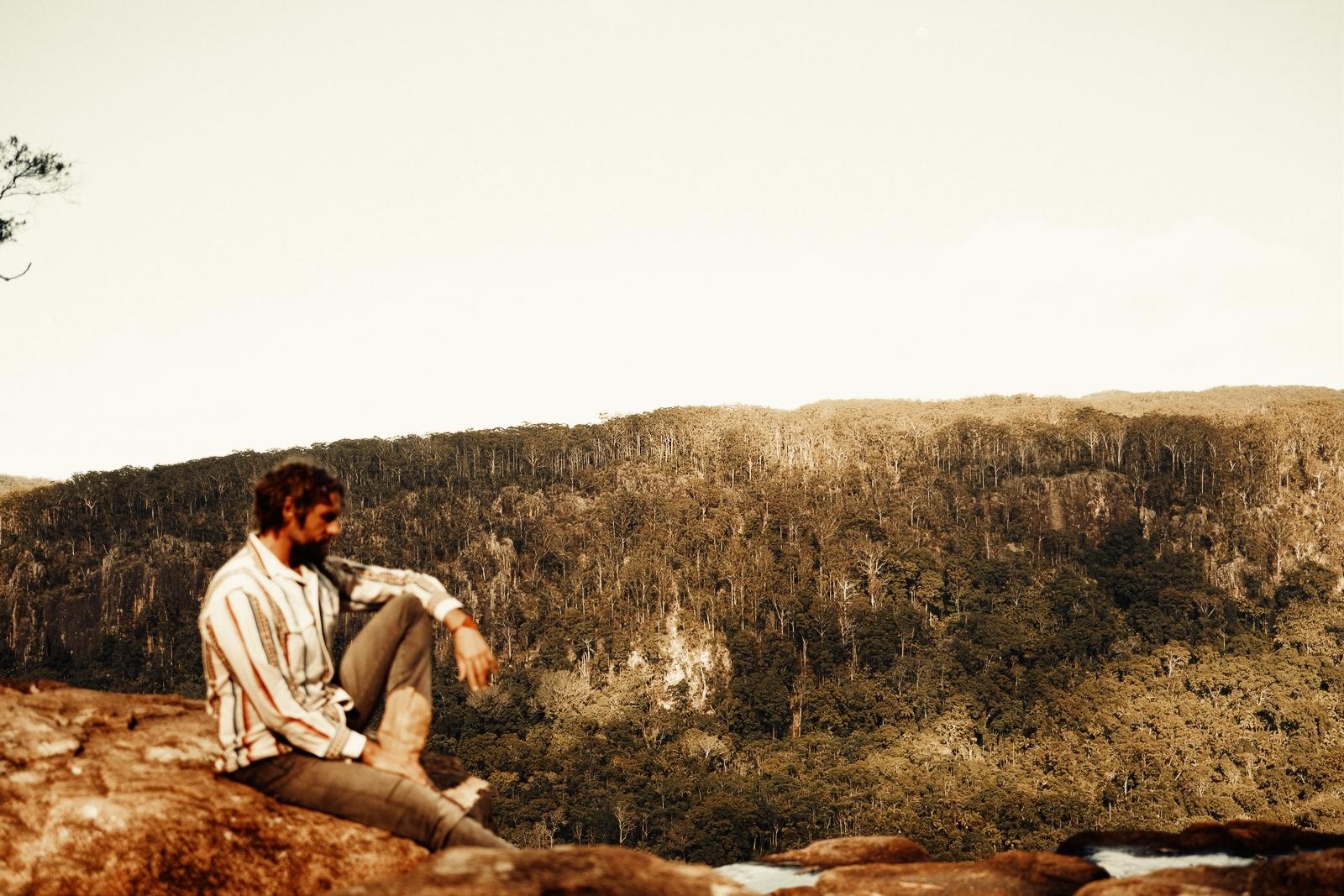Xuja sitting on a cliff edge overlooking a forested valley