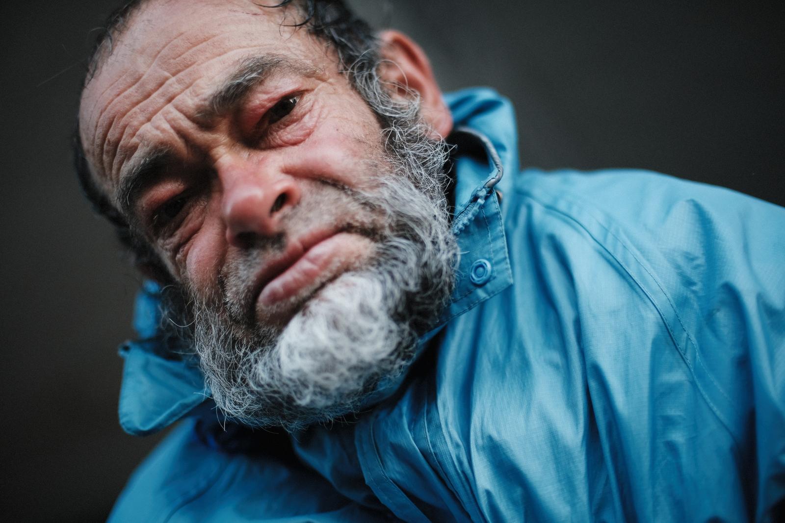 The man looking directly into the camera, head tilted, in a blue jacket