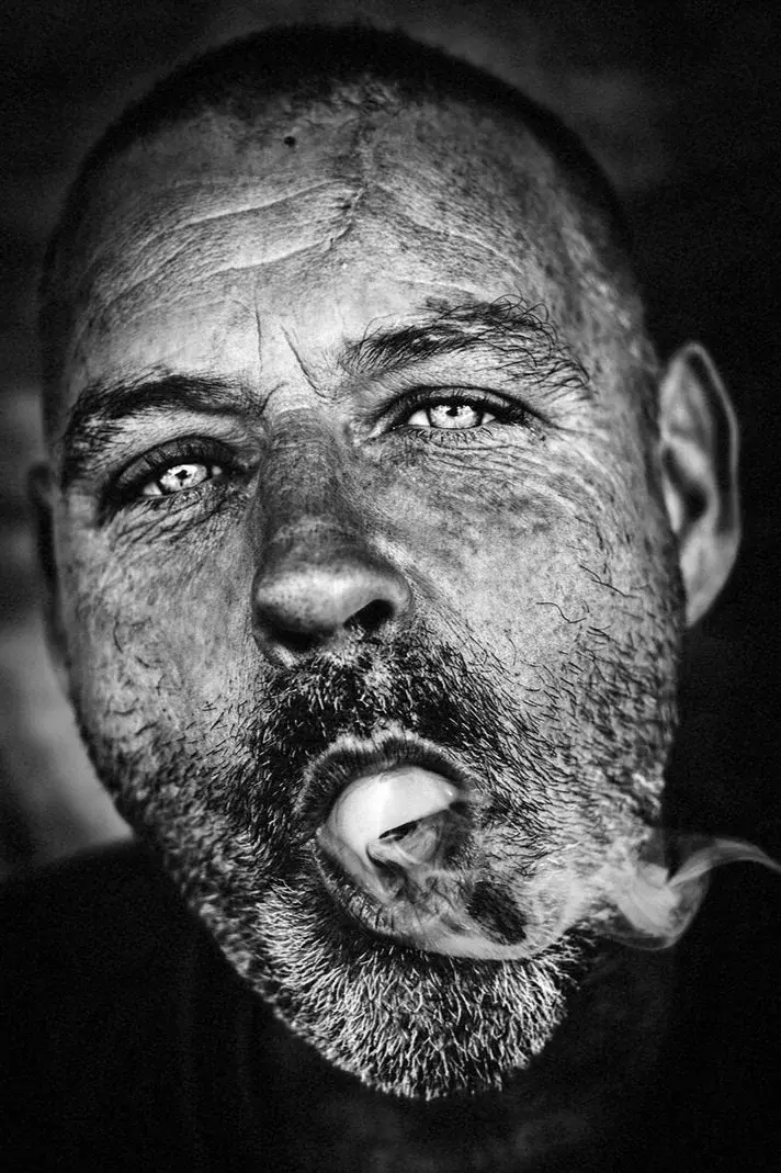 Close portrait of a bearded man exhaling smoke, intense pale eyes