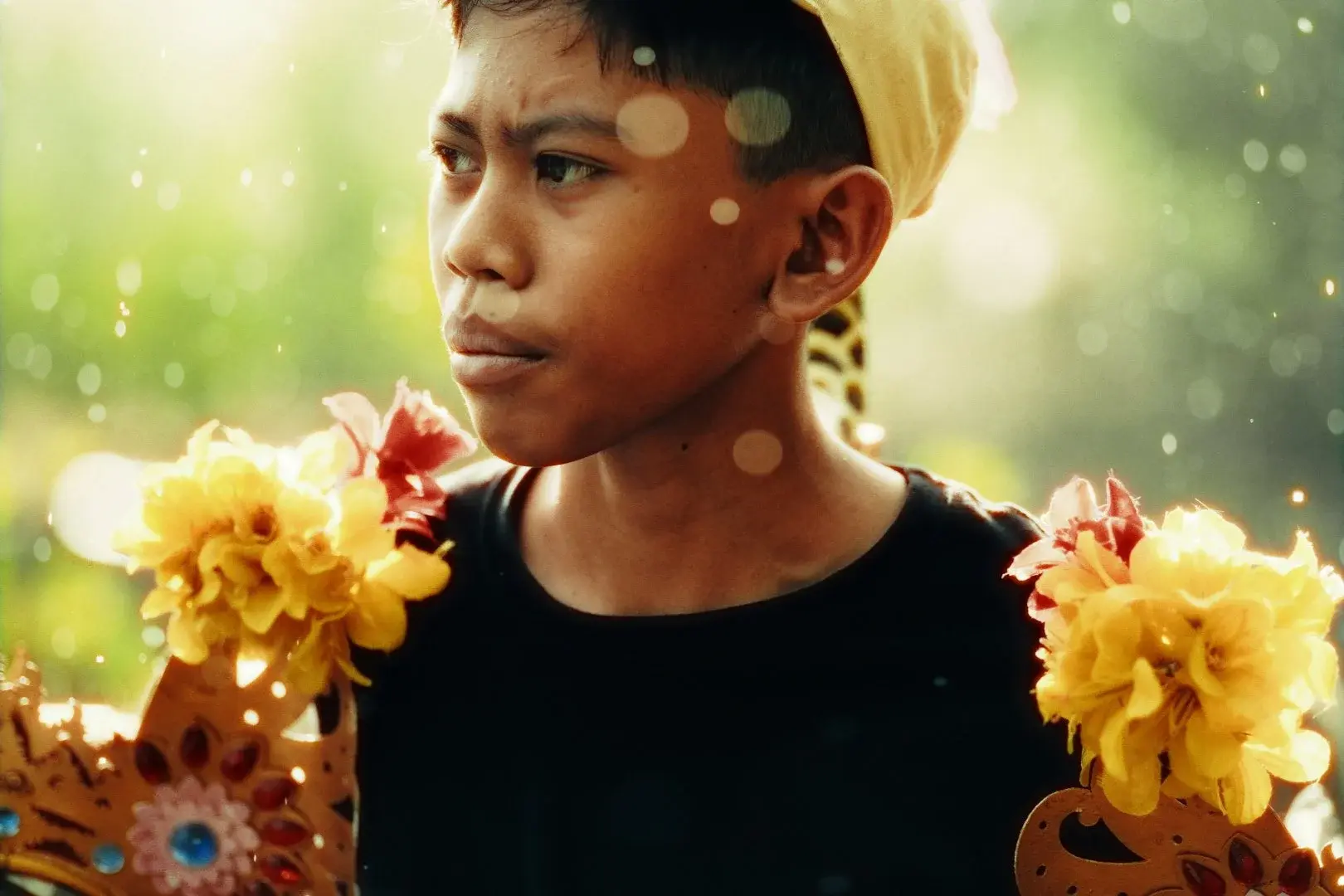 A boy in traditional Balinese ceremonial dress, backlit, holding a floral headdress