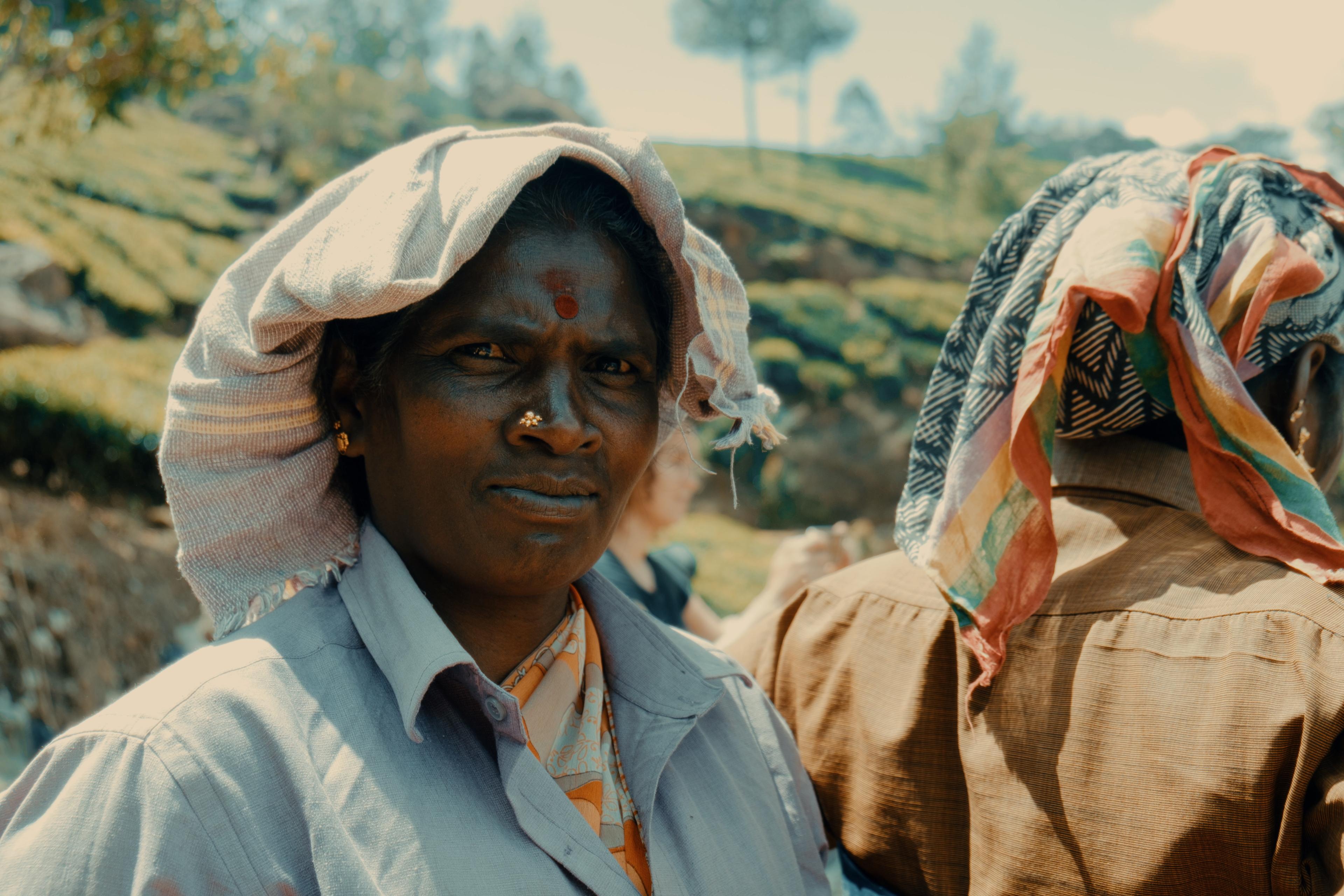 An older picker with a nose stud and gold earrings, another worker beside her