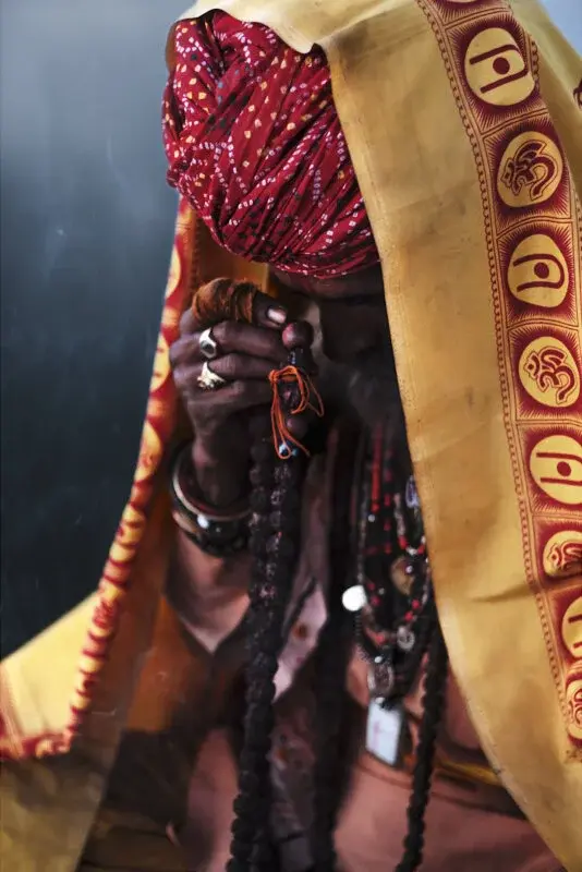 A sadhu wrapped in a yellow and red shawl, holding a string of prayer beads